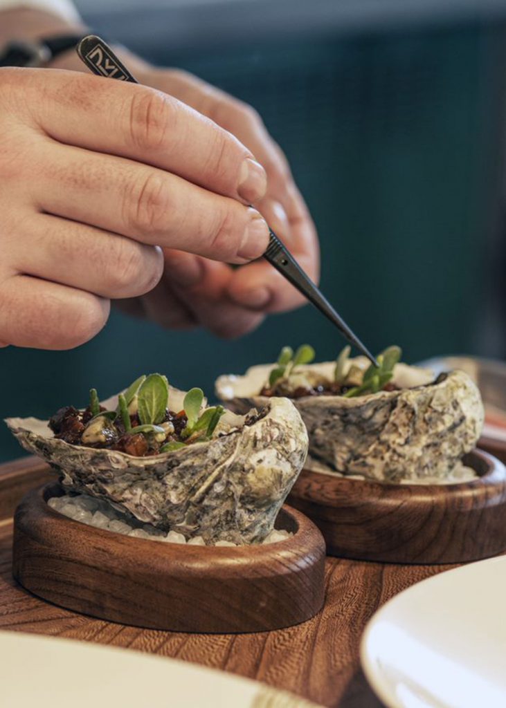 Hand holding tweezers placing microherbs on an oyster shell